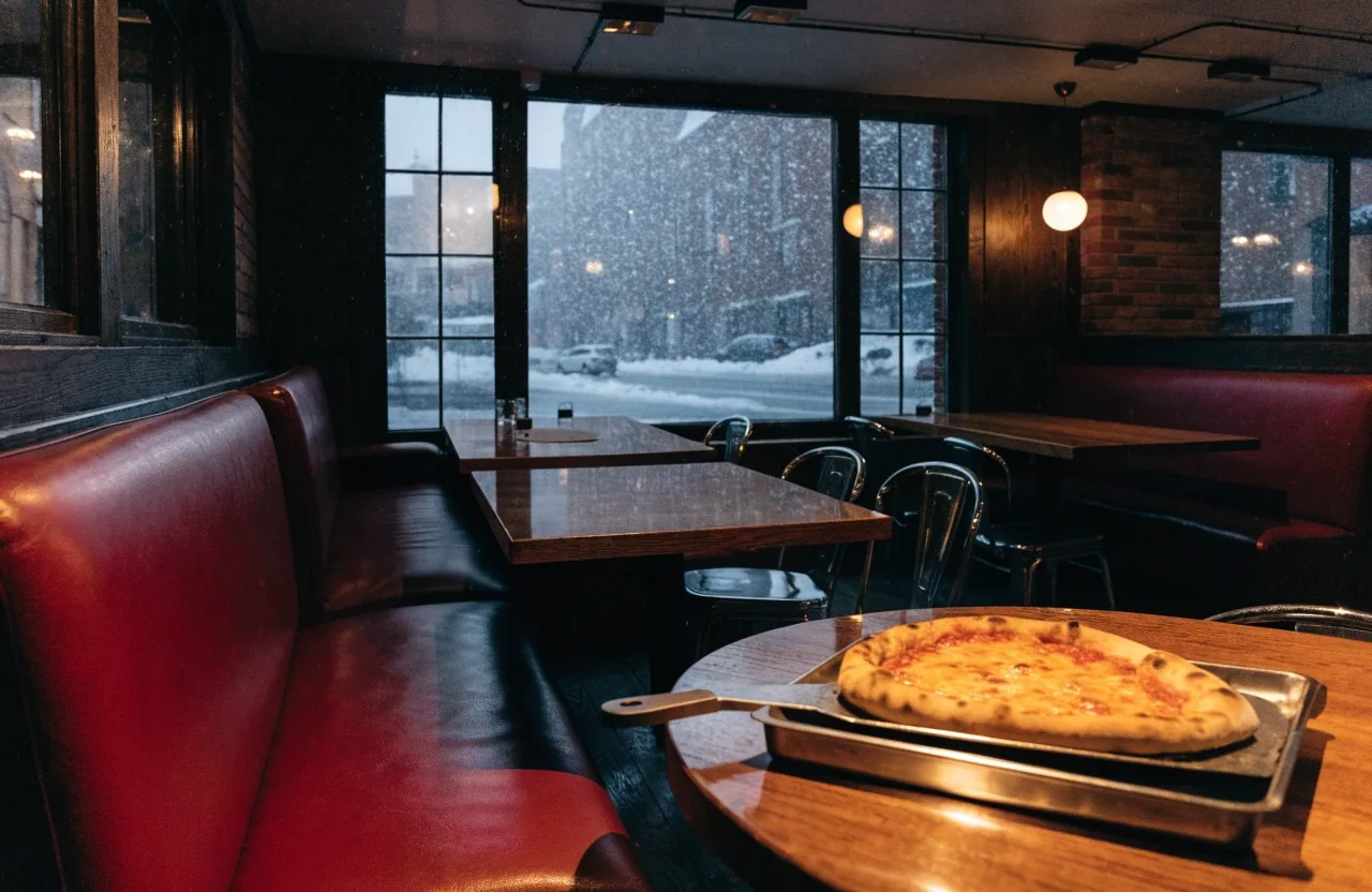 A dim neighborhood pizza restaurant interior at night with red vinyl seats and warm pendant lamps over the tables